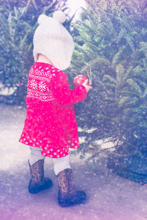 Cute baby girl in red Scandinavian dress at the Christmas tree farm.の写真素材
