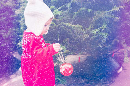 Cute baby girl in red Scandinavian dress at the Christmas tree farm.の写真素材