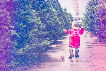 Cute baby girl in red Scandinavian dress at the Christmas tree farm.の写真素材