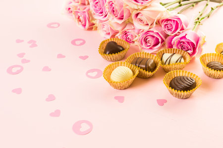 Assorted chocolates with pink roses on pink background.