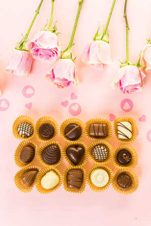 Assorted chocolates with pink roses on pink background.の写真素材