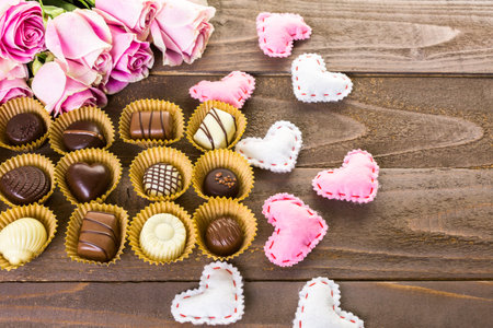 Assorted chocolated with pink roses on wood table.