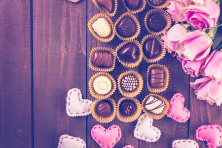 Assorted chocolates with pink roses on wood table.