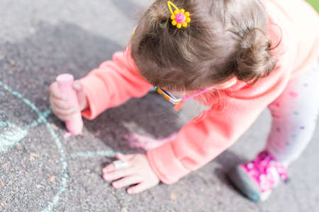 Toddler drawing with chalk on paved walk near playground.の写真素材