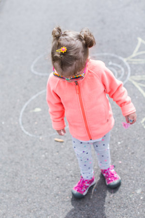 Toddler with chalk on paved walk near playground.の写真素材