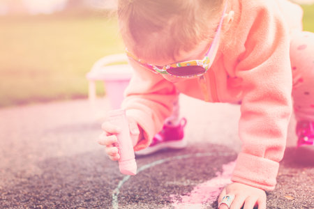 Toddler drawing with chalk on paved walk near playground.の写真素材