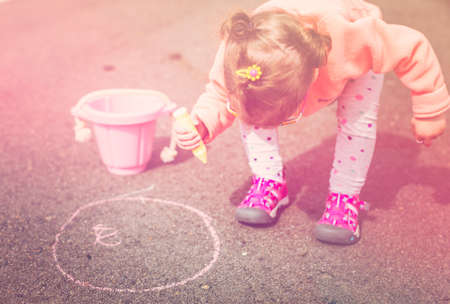 Toddler drawing with chalk on paved walk near playground.の写真素材