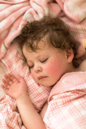 Cute toddler sleeping in her bed with pink bedding.の写真素材