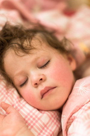 Cute toddler sleeping in her bed with pink bedding.の写真素材