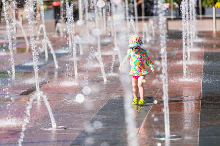 Toddler playing with small fountains on the urban plaza.の写真素材
