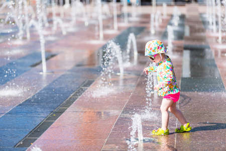 Toddler playing with small fountains on the urban plaza.の写真素材