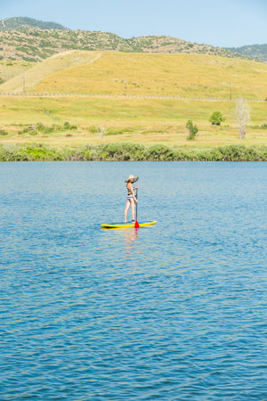 Young woman learning how to paddleboard on small pond.