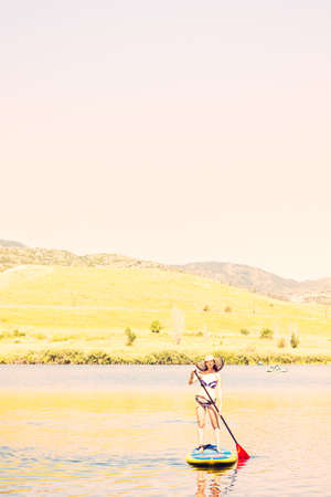 Young woman learning how to paddleboard on small pond.の写真素材