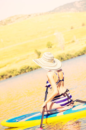 Young woman learning how to paddleboard on small pond.の写真素材