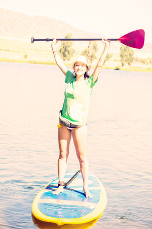 Young woman learning how to paddleboard on small pond.