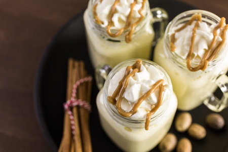 Traditional holiday drink egg nog garnished with caramel and whipped cream in drinking mason jars.の写真素材