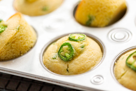 Freshly baked cornbread muffins with spicy jalapeno pepper in muffin pan.