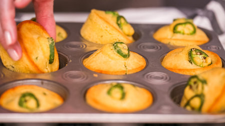 Step by step. Taking out freshly baked spicy jalapeno cornbread muffins from metal muffin pan.