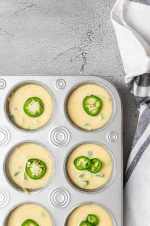Flat lay. Cornbread batter in muffin pans garnished with jalapeno peppers.