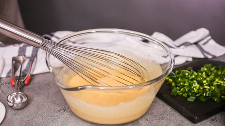 Step by step. Mixing ingredients together in glass mixing bowl for spicy jalapeno cornbread muffins.
