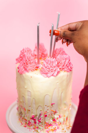 Woman putting birthday candles on pink and white buttercream cream cake with pink sprinkles and white chocolate ganache drip.の写真素材