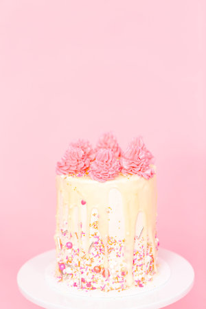 Pink and white buttercream cream cake with pink sprinkles and white chocolate ganache drip.の写真素材