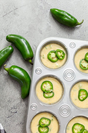 Flat lay. Cornbread batter in muffin pans garnished with jalapeno peppers.
