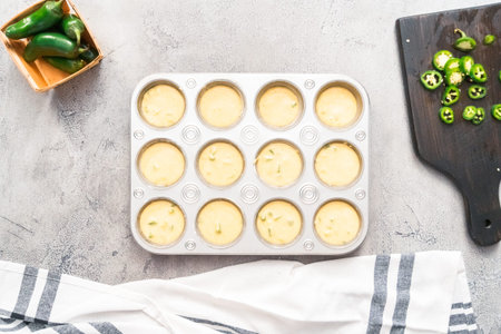 Flat lay. Cornbread batter in muffin pans garnished with jalapeno peppers.