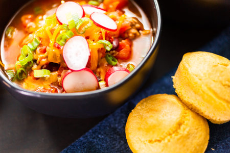 Close up of turkey chili garnished with fresh radishes, green onions and cheddar cheese.