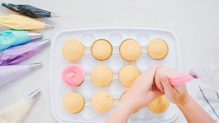 Step by step. Pastry chef piping butter cream frosting on unicorn cupcakes for little girl birthday...