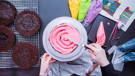 Step by step. Flat lay. Baker assembling a chocolate cake with bright colorful buttercream frosting...