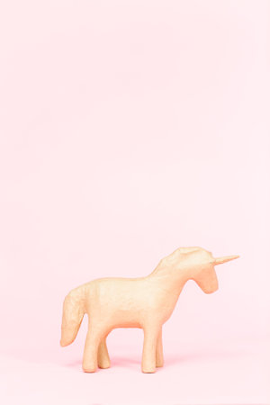 Unfinished paper mache figurine of unicorn on a pink background.