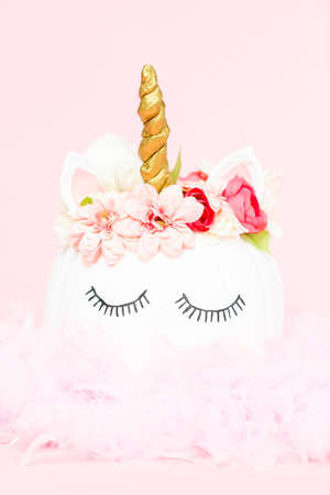 White unicorn pumpkin decorated with flowers on a pink background.の写真素材