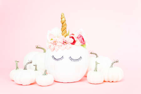 White unicorn pumpkin decorated with flowers on a pink background.の写真素材