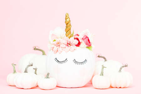 White unicorn pumpkin decorated with flowers on a pink background.の写真素材