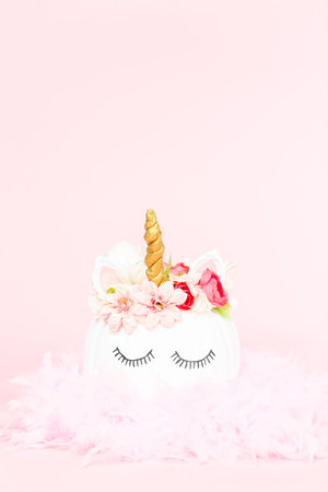 White unicorn pumpkin decorated with flowers on a pink background.の写真素材