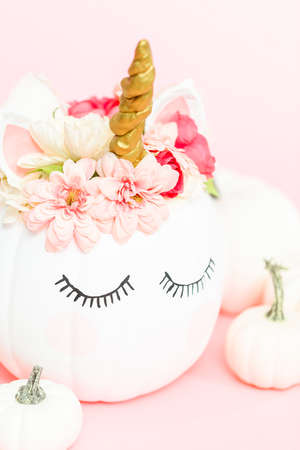 White unicorn pumpkin decorated with flowers on a pink background.の写真素材