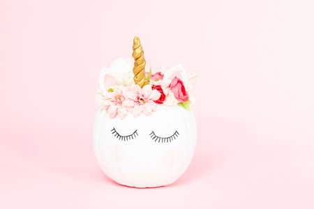 White unicorn pumpkin decorated with flowers on a pink background.の写真素材