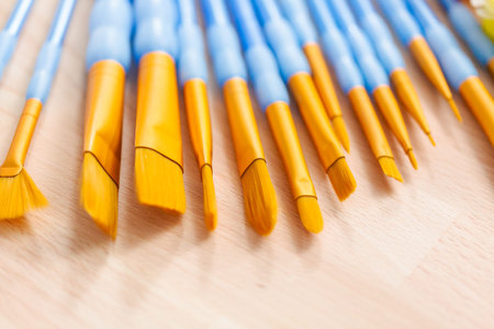 variety of new paint brushes with paint on a wood table.