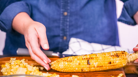 Step by step. Cutting the grilled corn of the cob ona wood cutting board.