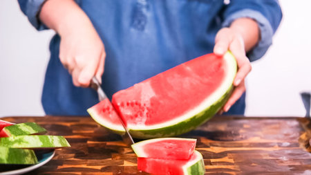 Slicing red woatermelon on a wood cutting board.の写真素材