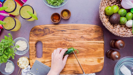 Step by step. Slicing fresh jalapeno pepper on a wood cutting board.