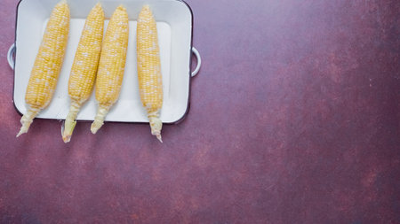 Step by step. Shucked organic corn on metal serving tray.