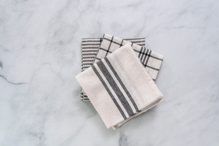 New kitchen towels with simple black pattern folded on marble counter.