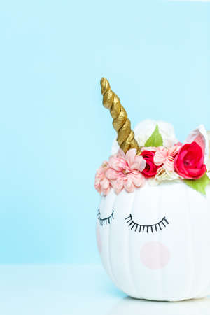 Craft pumpkin painted white and decorated with pink flowers as unicorn on blue background.の写真素材