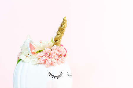 Craft pumpkin painted white and decorated with pink flowers as unicorn on pink background.の写真素材