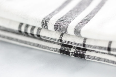 New kitchen towels with simple black pattern folded on marble counter.
