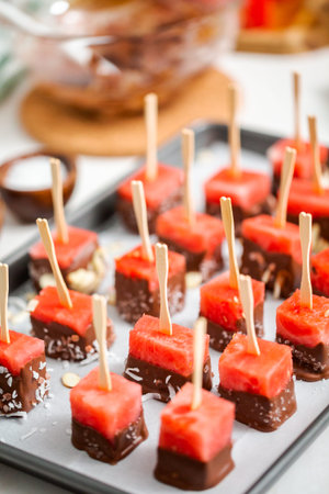 Preparing watermelon appetizers dipped in chocolate and sprinked with sea salt and almonds.