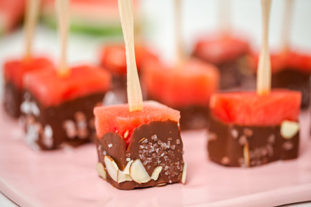 Preparing watermelon appetizers dipped in chocolate and sprinked with sea salt and almonds.