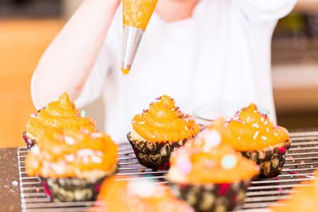 Little girl decorating orange icing on cupcakes with sprinkle mix.の写真素材